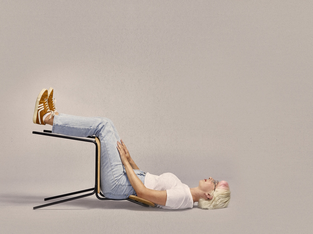 Lady with blonde hair sitting on a chair while lying on the ground