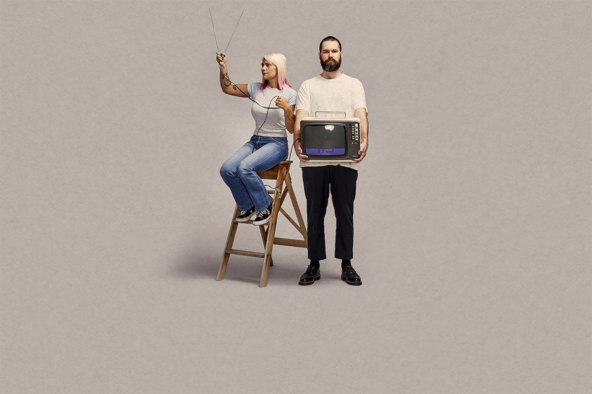Man holding old fashioned TV, woman standing next to him holding antenna up