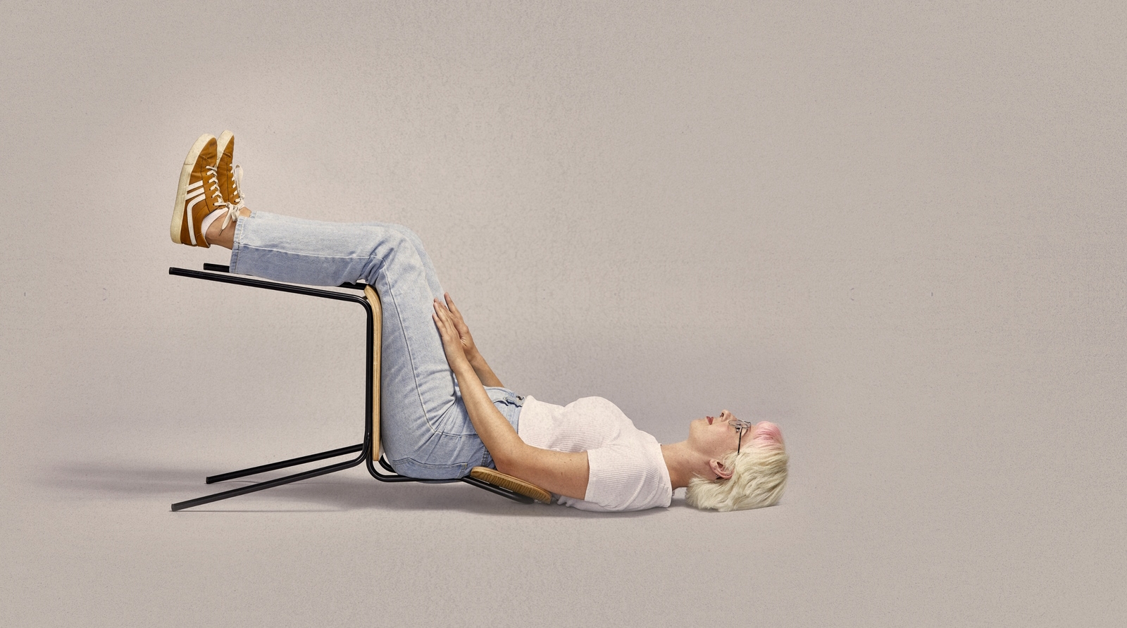 Lady with blonde hair sitting on a chair while lying on the ground